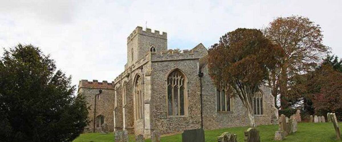 A historic stone church with a tower and arched windows, surrounded by a cemetery with headstones.