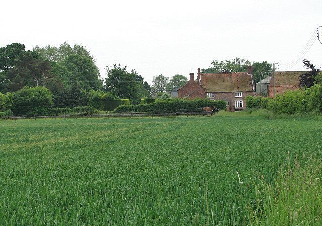 A rural landscape with a green field, a brick house, and trees in the background.
