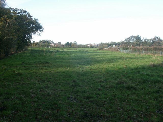 Un campo cubierto de hierba con árboles y una valla al fondo.