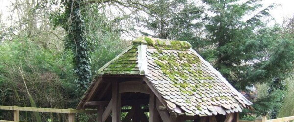 A rustic wooden structure with a tiled roof, surrounded by a wooden fence and a gravel path.