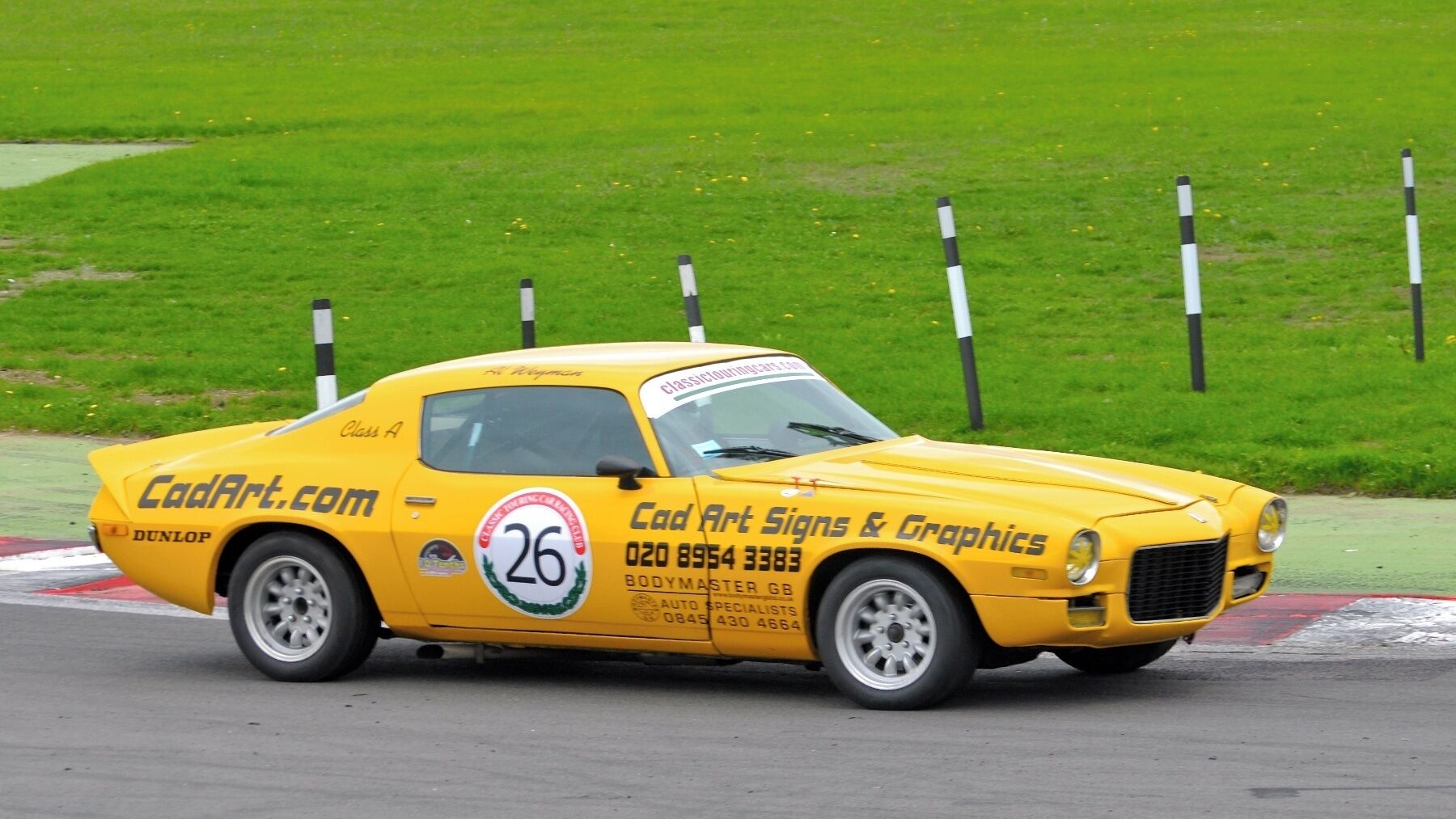 A yellow classic car with racing decals on a track.