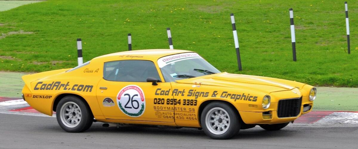 A yellow classic car with racing decals on a track.