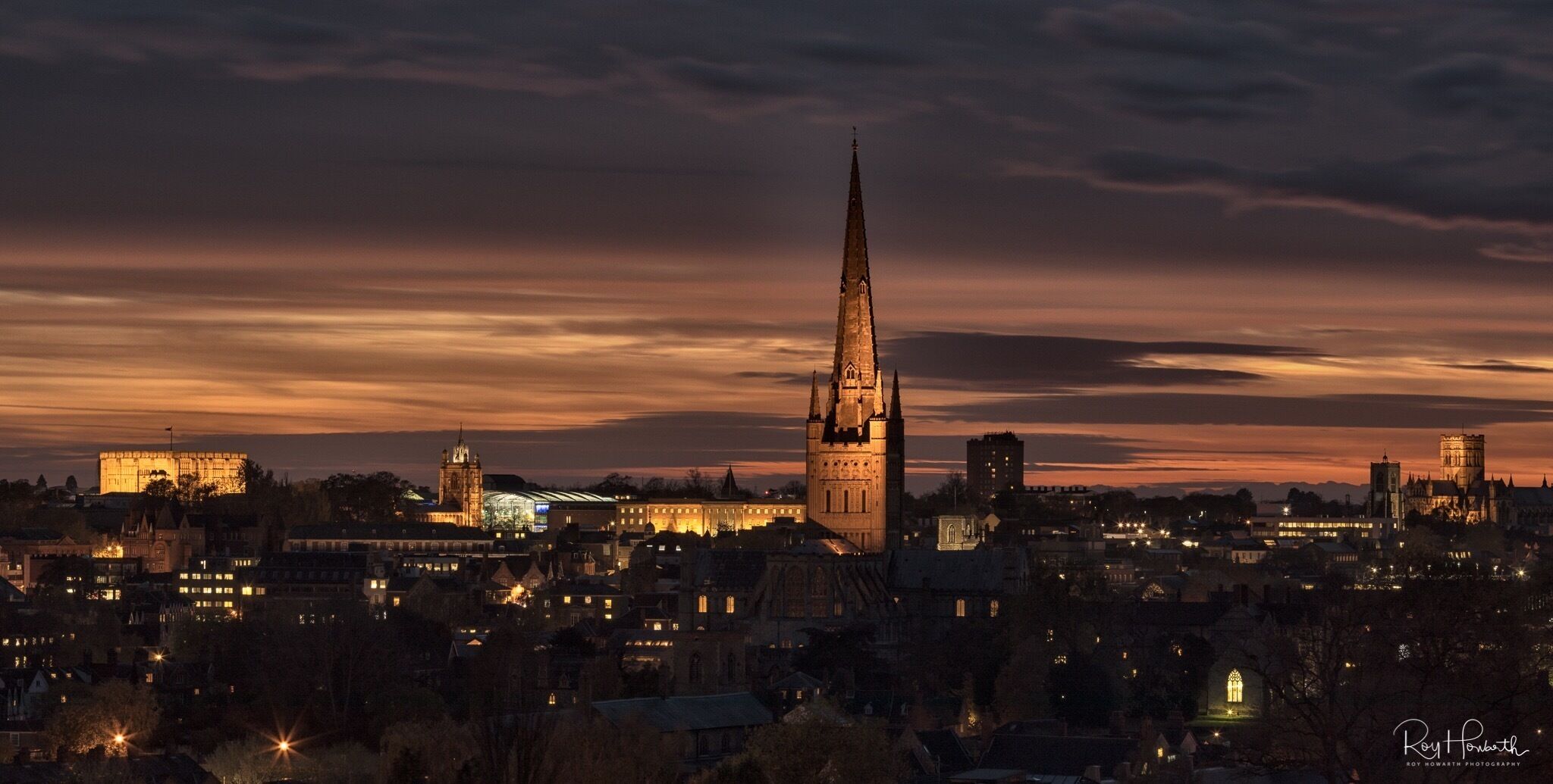 A cityscape at dusk with a prominent church spire and illuminated buildings.
