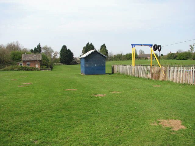 A grassy field with a blue shed, a wooden fence, and a blue swing set.