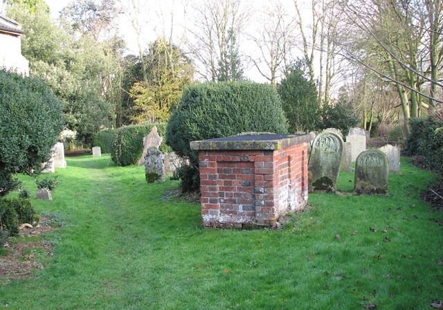 A cemetery with gravestones, a brick structure, and well-maintained greenery.