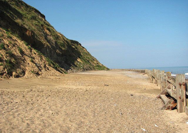 A sandy beach with a wooden fence and a rocky cliff.