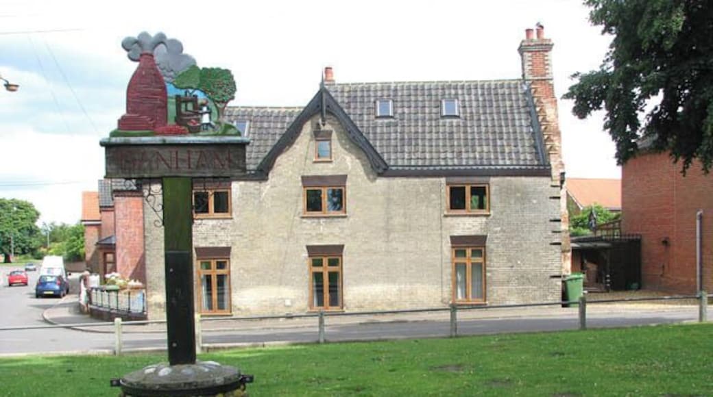 Banham - the village sign. The village sign > 1408844 is located on the green by Church Hill. Perhaps most widely known for its renowned zoo, the village of Banham is located along the B1113, 11 kilometres north of Diss, 19 kilometres east of Thetford and 32 kilometres south-west of Norwich. The tree-lined village green > 1408840 is surrounded by old thatched houses > 1408825 some with overhanging storeys, and dominated by St Mary's church > 1408886 which adjoins the green in the west. Industries in Banham include the Gaymer Cider factory and brick making from locally found clay. The village has a number of small shops, a Spar supermarket and a village shop > 1408855 and post office, two pubs, and a primary school which caters for about 120 pupils.