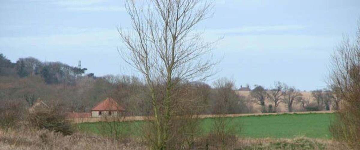 A river flowing through a rural landscape with fields, a leafless tree, and a small building in the background.