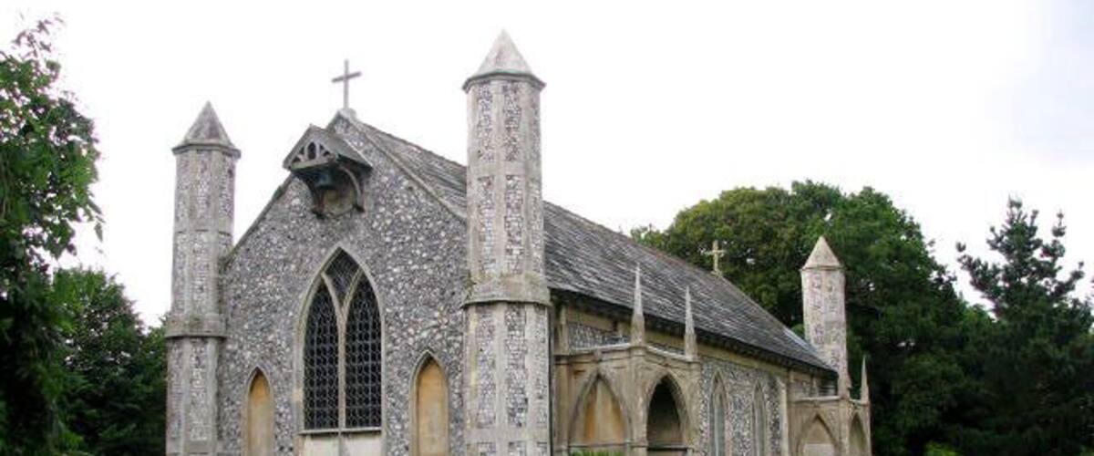 A stone church with a cross on the roof, surrounded by greenery.