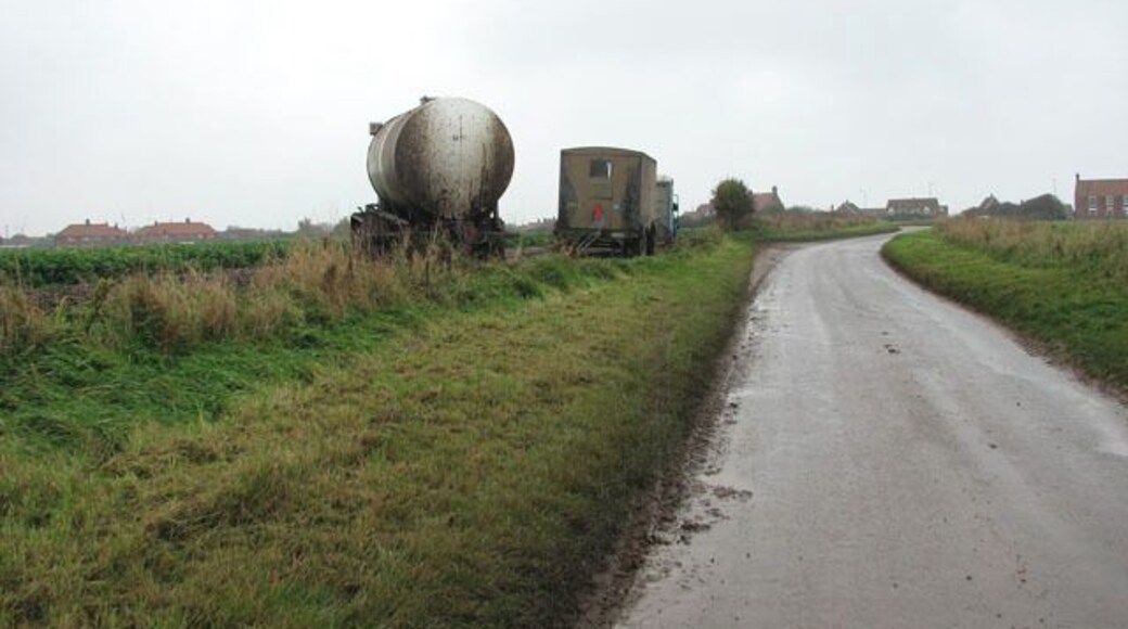 View north along Mill Common Road. The northernmost section of which is called Ridlington Road > 1036299. Various trailers, bits of machinery and mobile toilets can be seen parked on the field edge at left, where the parsnip harvest is in progress. The parsnips are processed in a mobile unit on the field > 1036298.