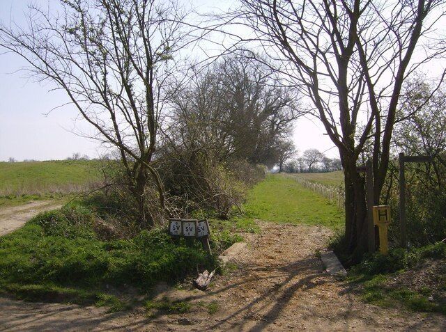 Inviting footpath From the road, which turns from east to north at this point, a footpath goes right (south) and this one continues east towards Brundish. The bank to the left is the bank of a reservoir which is partly in this square. A new reservoir, not yet shown on maps, has also been constructed to the right behind a line of saplings along the path. The presence of the reservoirs probably explains the proliferation of hydrant and stop valve signs here.