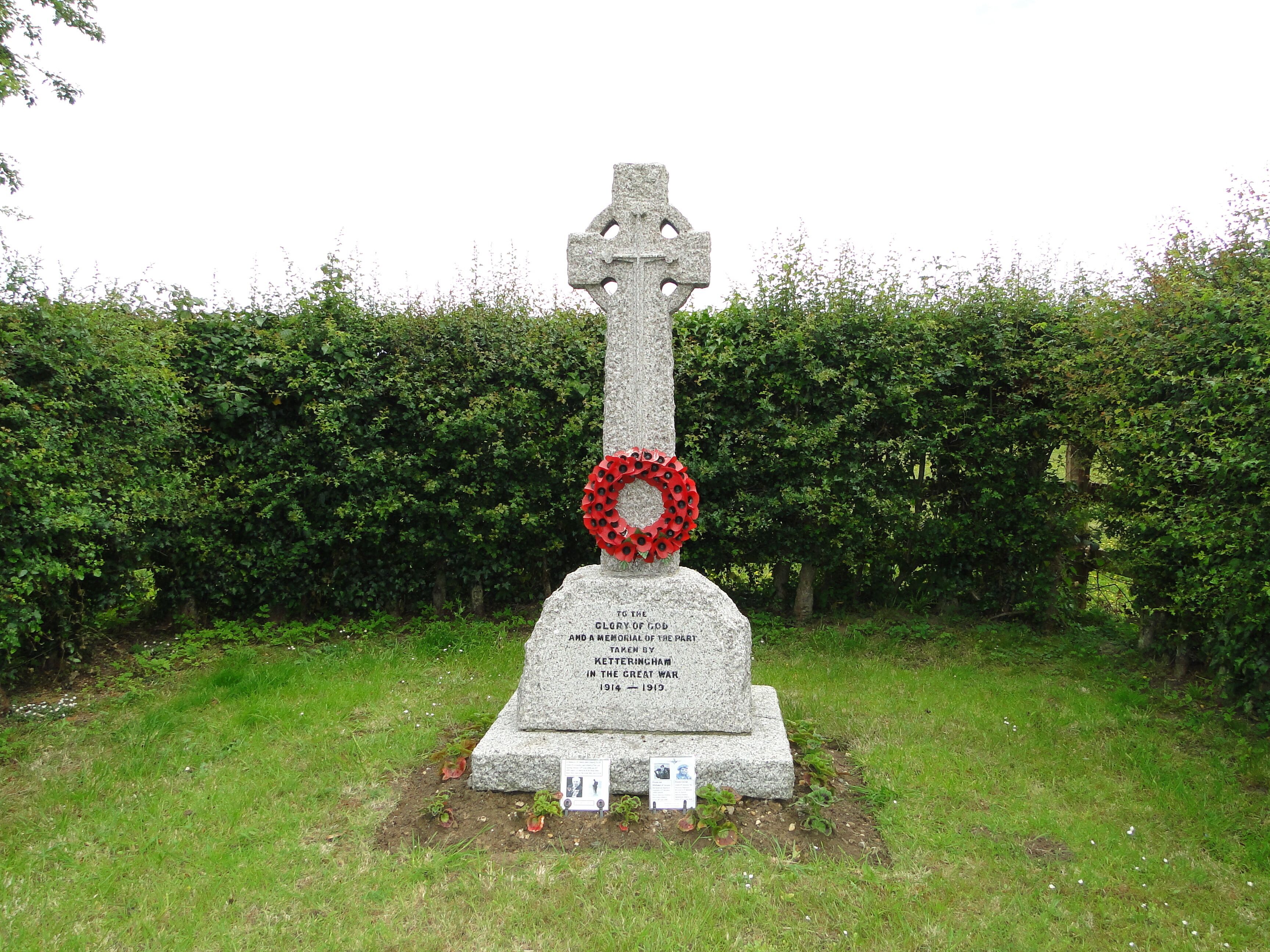 A stone cross with a red poppy wreath and a memorial plaque.