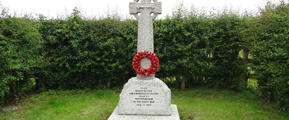 A stone cross with a red poppy wreath and a memorial plaque.