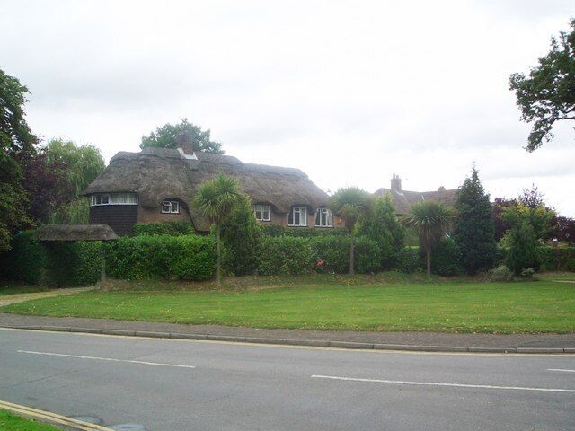 A house with a thatched roof, surrounded by a well-maintained lawn and a road in the foreground.
