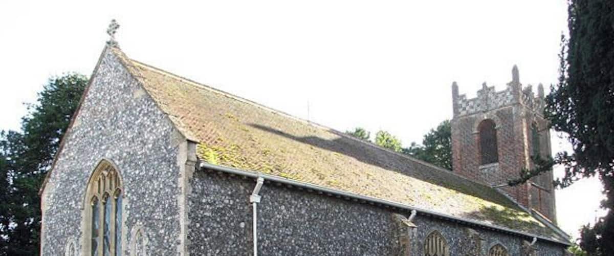 A stone church with a bell tower and a hedge in front.