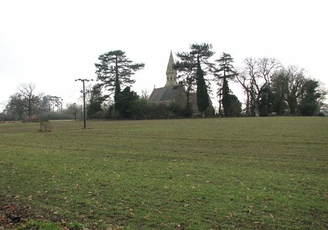 A grassy field with a church and tall trees in the background.