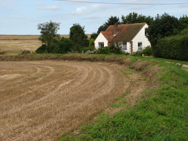 A rural landscape with a white house, a field of harvested crops, and a clear sky.