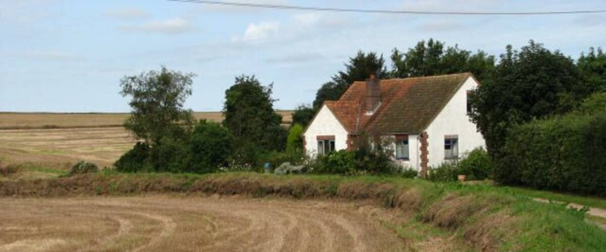 A rural landscape with a white house, a field of harvested crops, and a clear sky.
