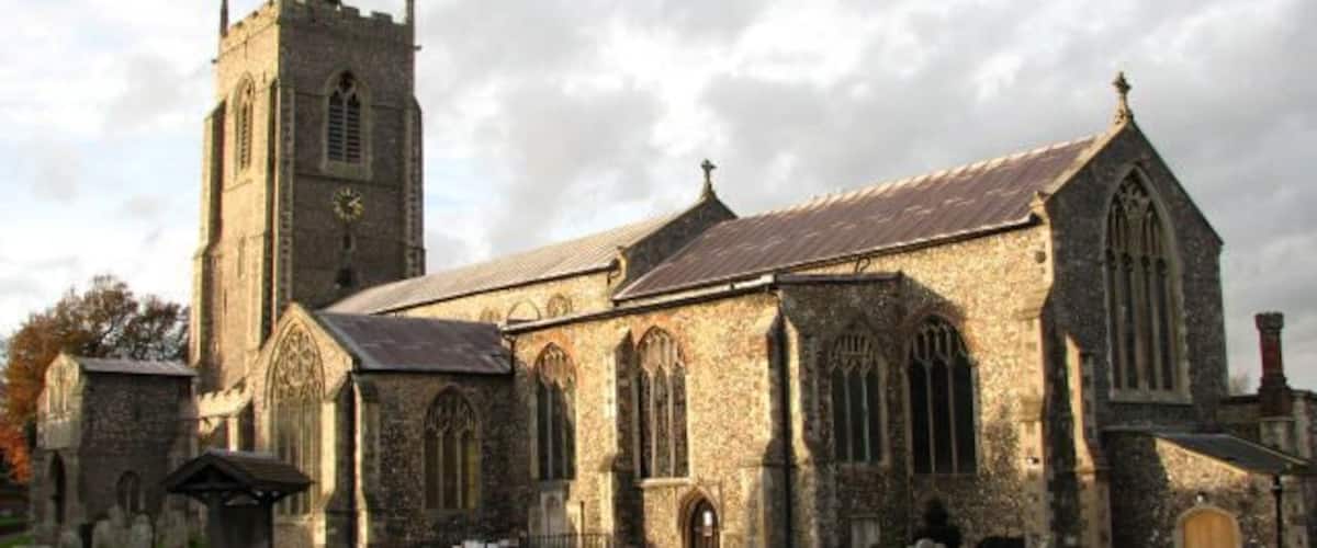 Una iglesia histórica con una alta torre y un cementerio frente a ella.
