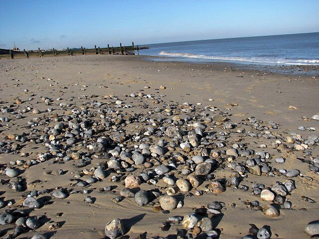 View NW on Walcott Beach The tide is out and pebbles are exposed in the drying sand of the beach.
