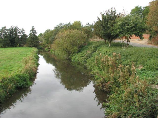A narrow waterway flanked by grassy banks and trees.