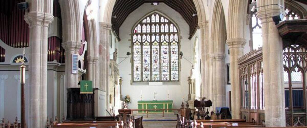 A church interior with wooden pews, a blue carpet, and a large stained glass window.