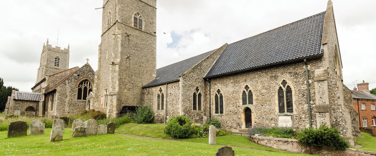 A historic stone church with a tall tower and a cemetery in front.