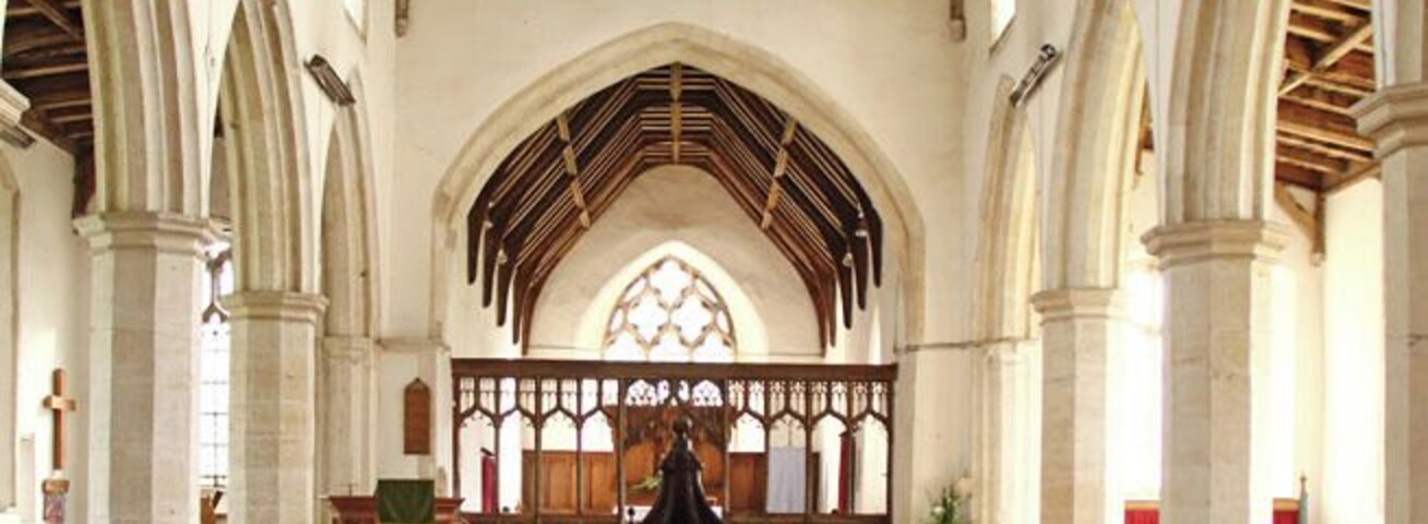Interior de iglesia con techos abovedados, bancos de madera y una fuente de piedra central.