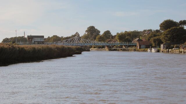 A river with a bridge, a house, and trees in the background.