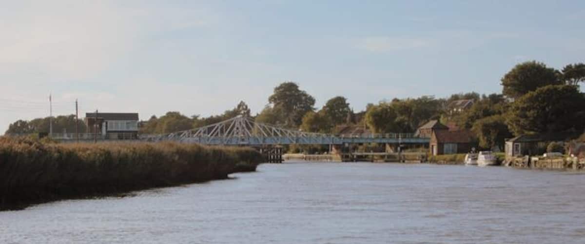 A river with a bridge, a house, and trees in the background.