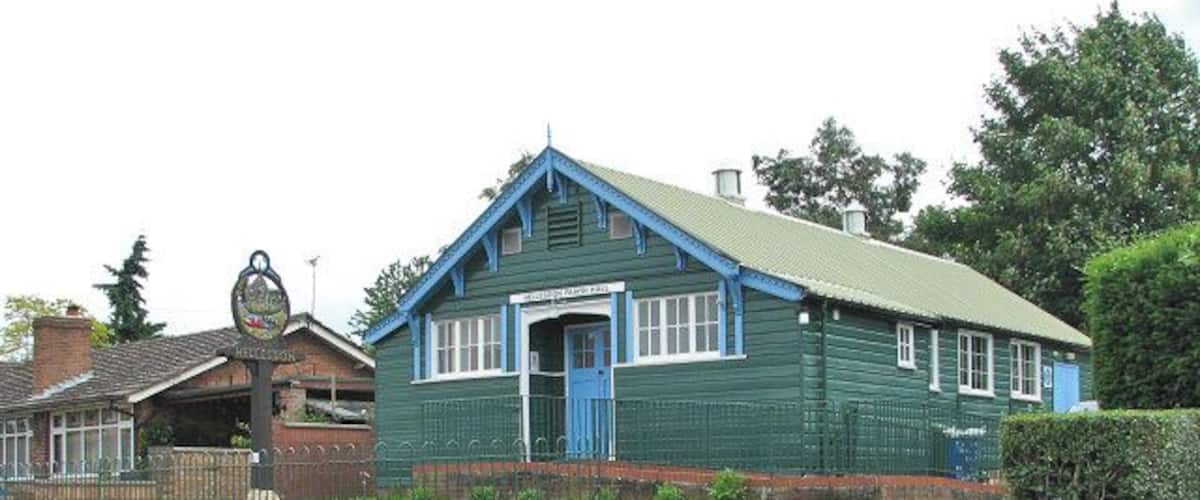 A green building with a blue door and windows, surrounded by a fence and greenery.