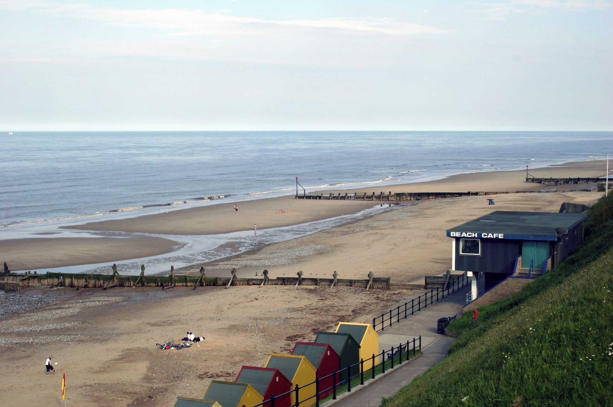 A beach with a pier, a beach cafe, and colorful beach huts.
