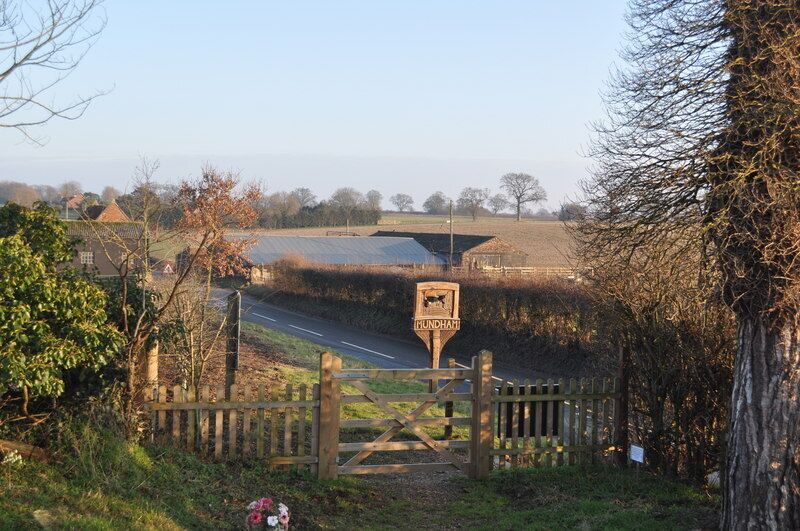 A rural road with a wooden gate and a signpost.