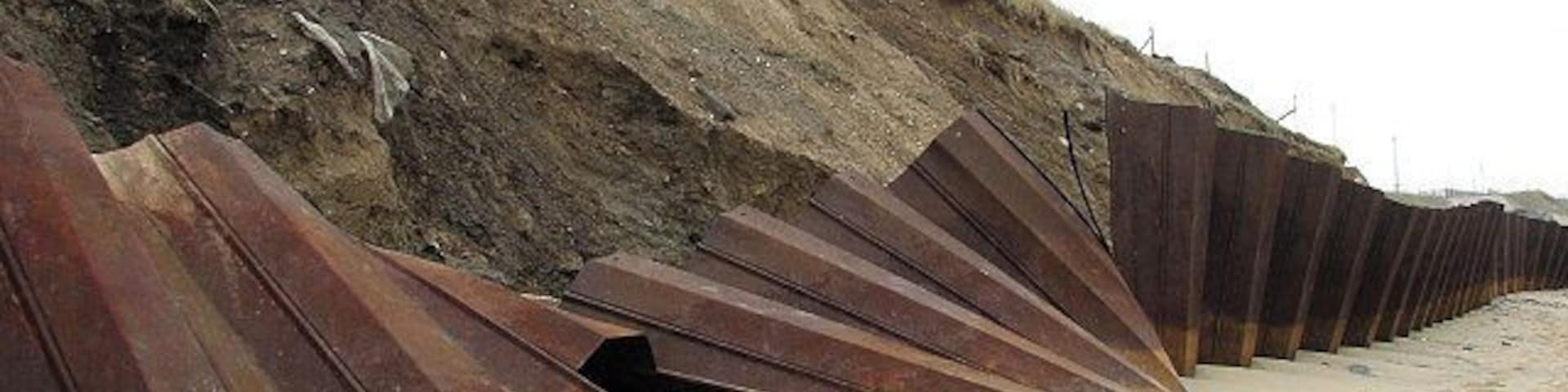 Uma praia com grandes chapas de metal enferrujado empilhadas em fileiras.