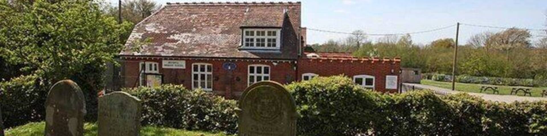 A red brick house with a tiled roof, surrounded by a grassy area with two headstones.