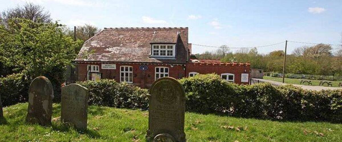 A red brick house with a tiled roof, surrounded by a grassy area with two headstones.