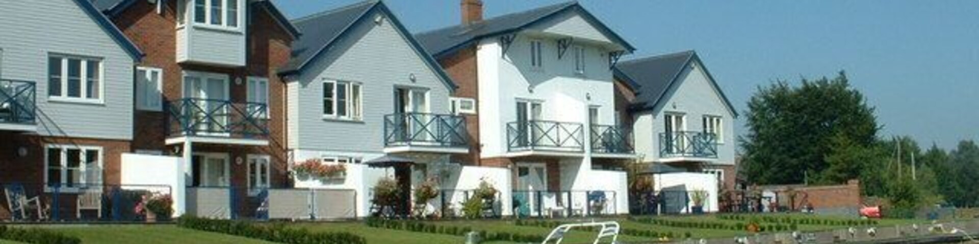 Filas de casas modernas junto a un río tranquilo con barcos amarrados.