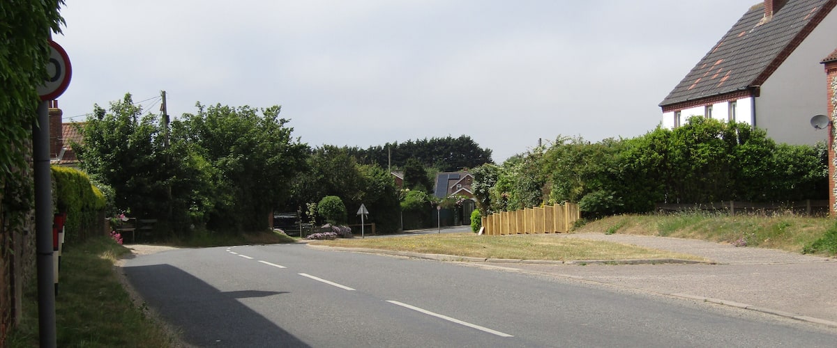 A quiet rural road with a house on the right and a signpost on the left.