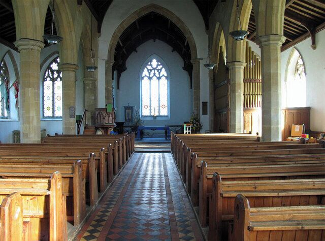 An interior of a church with wooden pews, a tiled floor, and a large stained glass window.