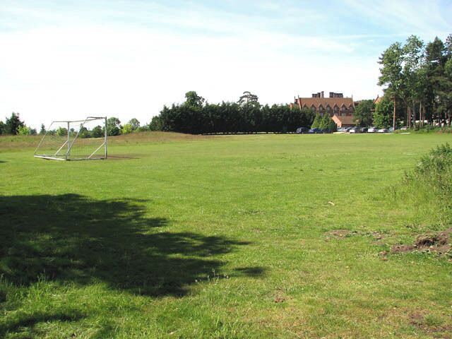 A grassy field with a soccer goal, trees, and a building in the background.