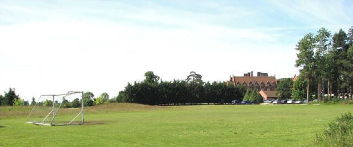 A grassy field with a soccer goal, trees, and a building in the background.