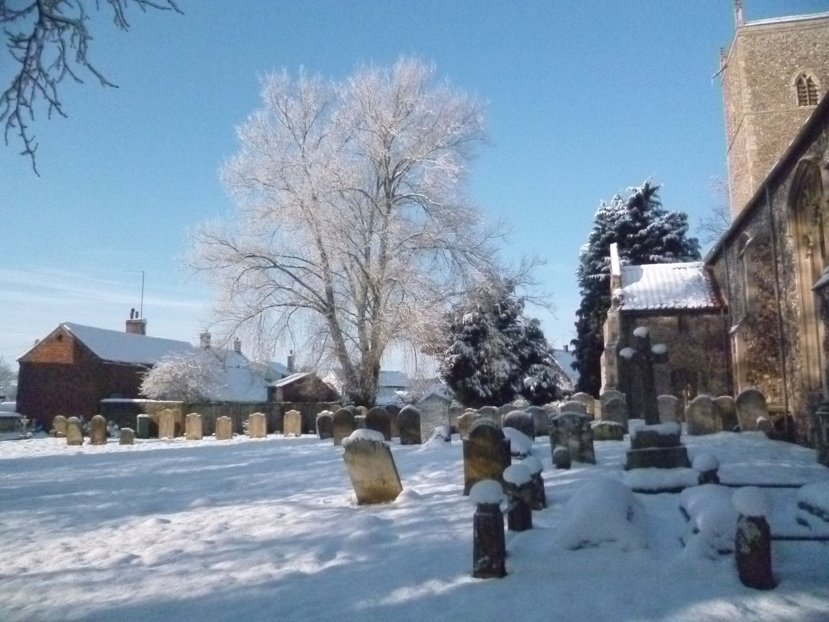 A cemetery with snow-covered gravestones and a church in the background.