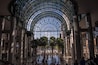 Un vaste atrium doté d’un plafond en forme de dôme de verre, de palmiers et d’un sol réfléchissant.