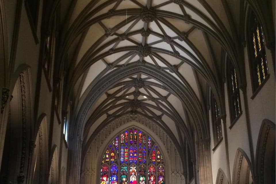 A Gothic-style cathedral interior with a high vaulted ceiling and stained glass windows.