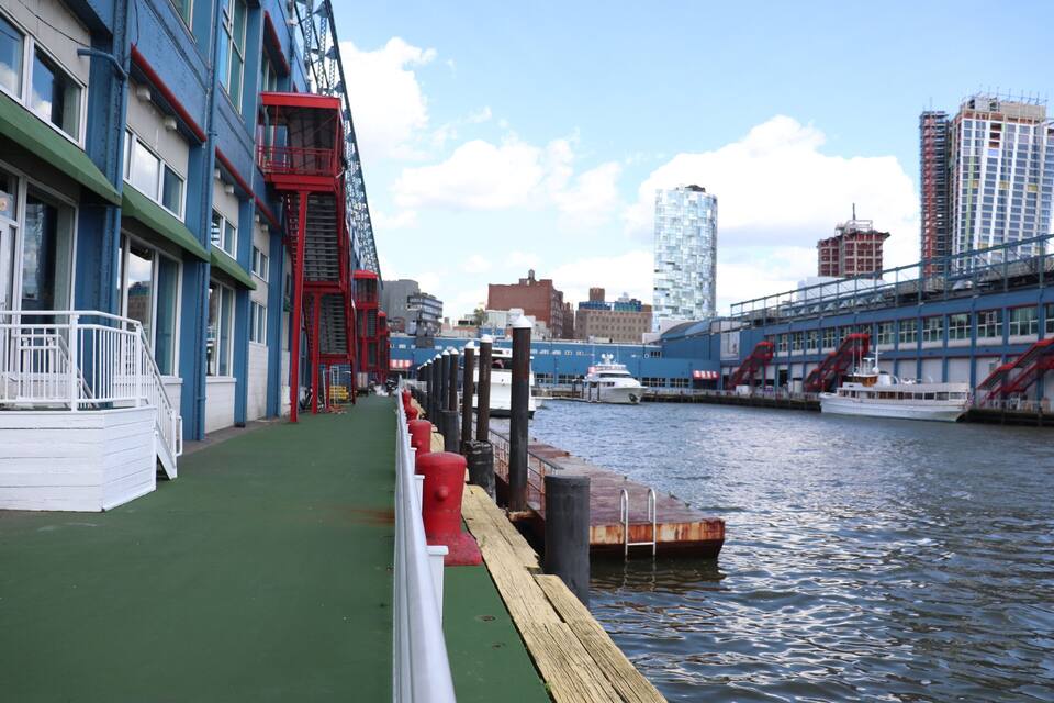A waterfront promenade with a green walkway, red fire escape, and a dock with boats.
