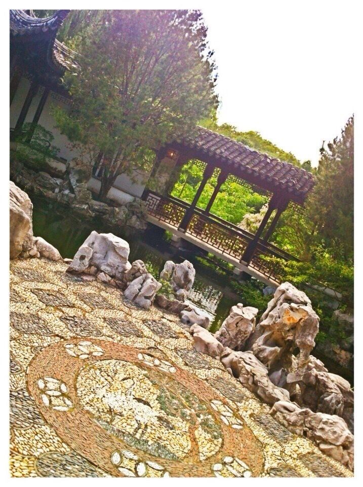 Un chemin en mosaïque, un pont en bois et un pavillon dans un jardin.