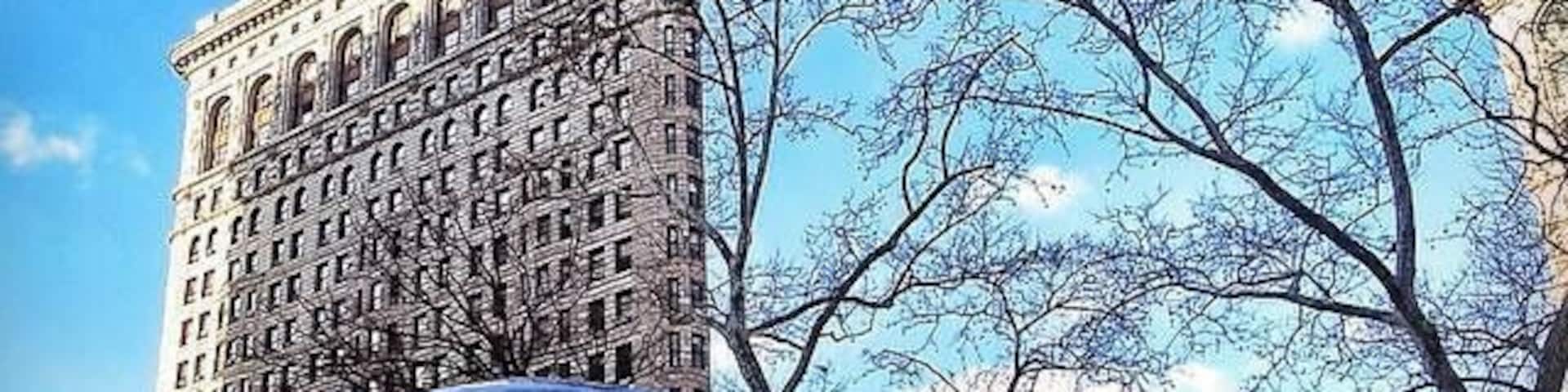 Una gran esfera de vidrio que refleja un paisaje urbano, con un edificio alto al fondo y un árbol en primer plano.