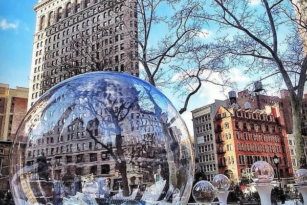A large glass sphere reflecting a cityscape, with a tall building in the background and a tree in the foreground.