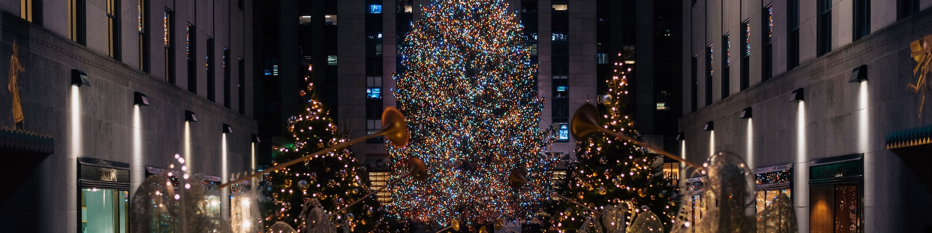 Uma grande árvore de Natal iluminada em uma praça da cidade, cercada por edifícios.