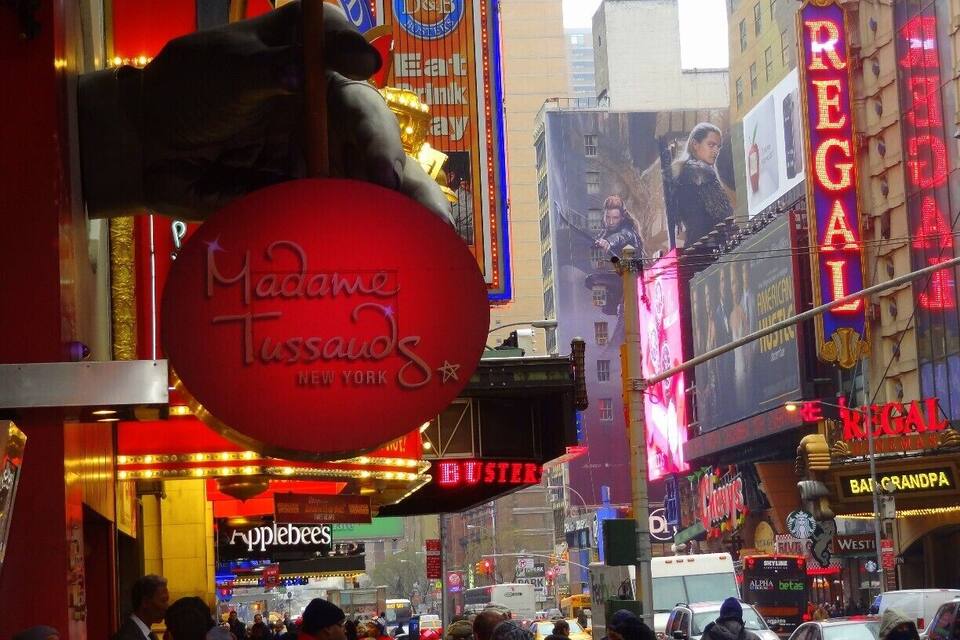 Times Square with prominent billboards and neon signs, including 'Madame Tussauds' and 'Regal'.